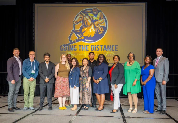 A group of people standing in front of a banner reading “going the distance”.