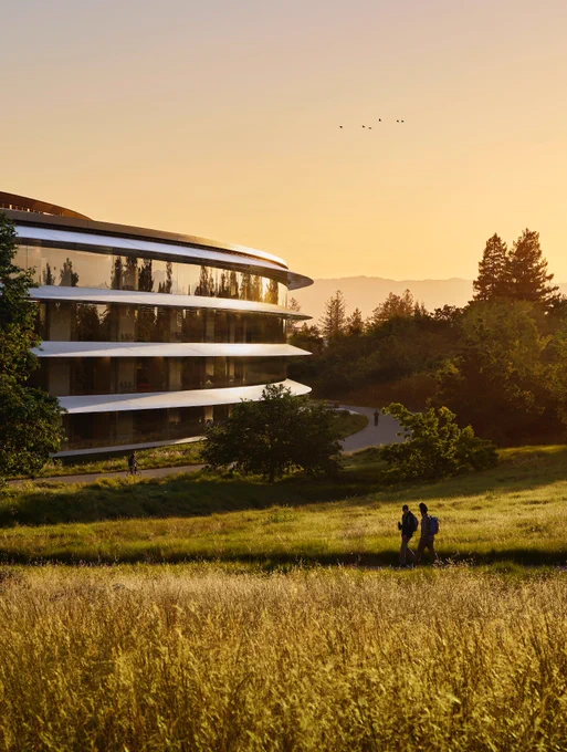A photo of Apple Park at sunrise, with people walking and riding bikes along the path.