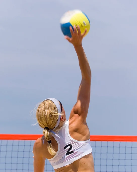 A female beach volleyball player mid air.