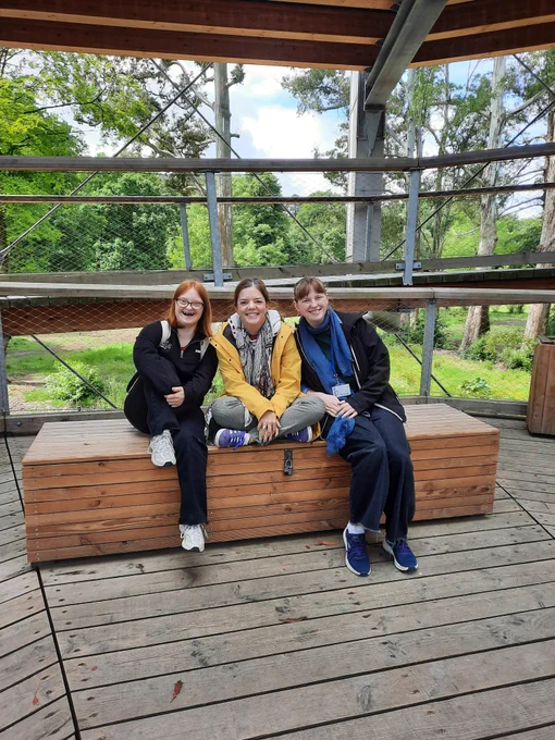 3 people sitting on a wooden bench at the bottom of a spiral walkway