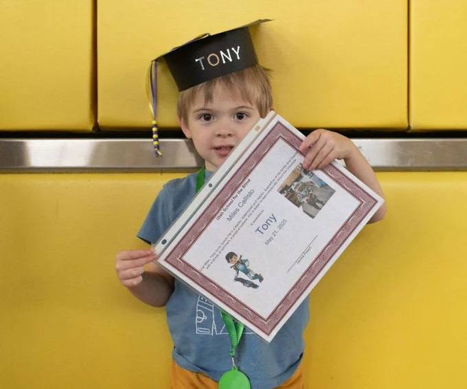 a boy stands in front of a yellow background with a grad cap with the name tony written on it. he holds a certificate also with his name up in front of him.