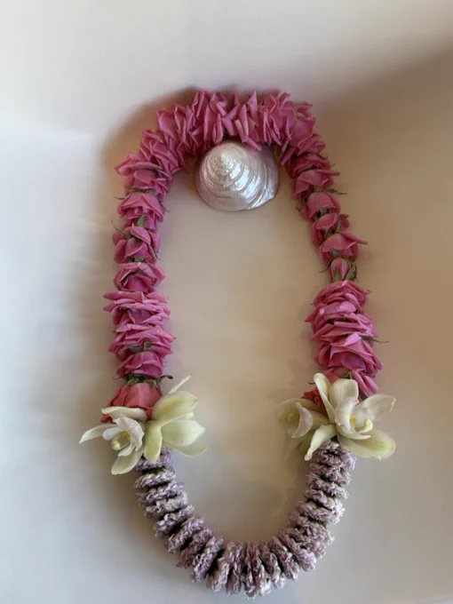 A traditional Hawaiian lei made of pink and white flowers, displayed in a loop with a white shell at the top center, on a light background.