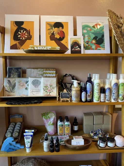 A display shelf containing a variety of products, including artwork made by a Hawaiian artist, assorted natural skincare items, handcrafted soap bars, and other sustainably sourced products sold in a small, local boutique.
