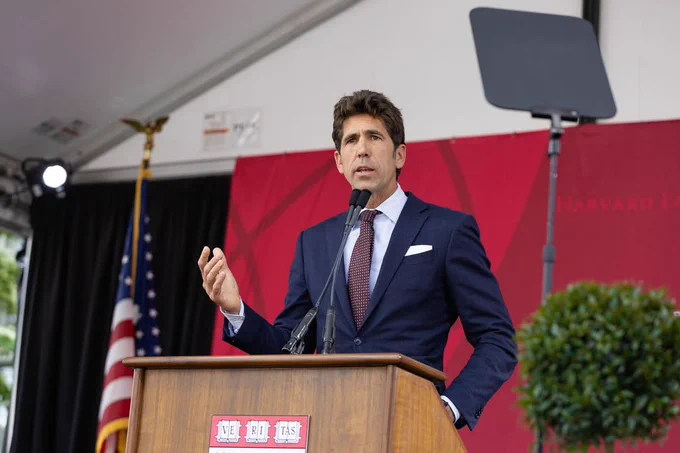 Bob Myers speaking at a podium with a Harvard Law School banner in the background.