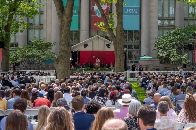 Outdoor graduation ceremony at Harvard Law School, with audience seated facing a stage under a white canopy.