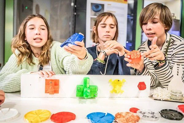 photographie de trois élèves lors de l’édition de Jeunes Makers 2024. Les élèves montrent des objets imprimés en 3D de différentes couleurs. Des objets imprimés en 3D sont également posés sur la table. 