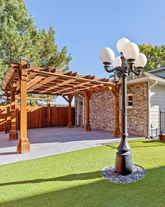 A well-maintained backyard featuring a wooden pergola and artificial turf, with a vintage street lamp in the foreground.