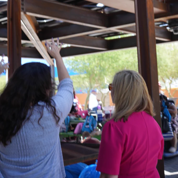 Two people are taking a photo under a steel structure. A crowd is visible in the background.
