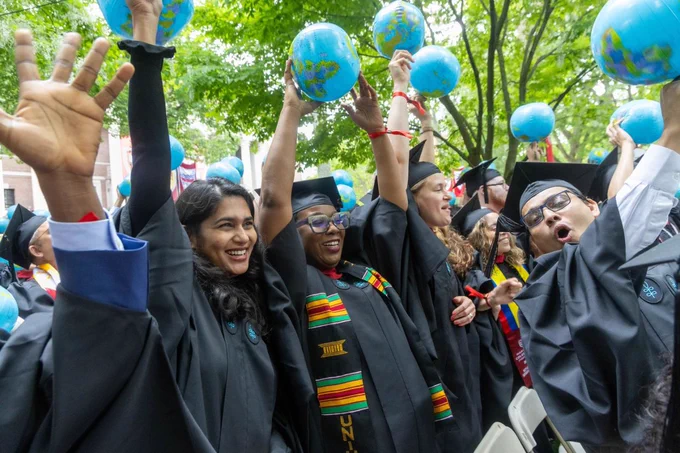 Graduates cheering and holding inflatable globes in the air.