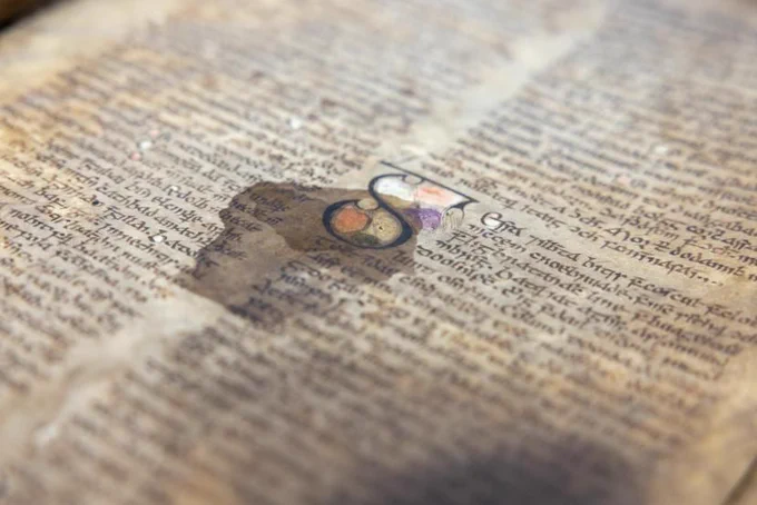 Old manuscript covered in lines of medieval Irish script written in black ink, with an decorative S in the centre