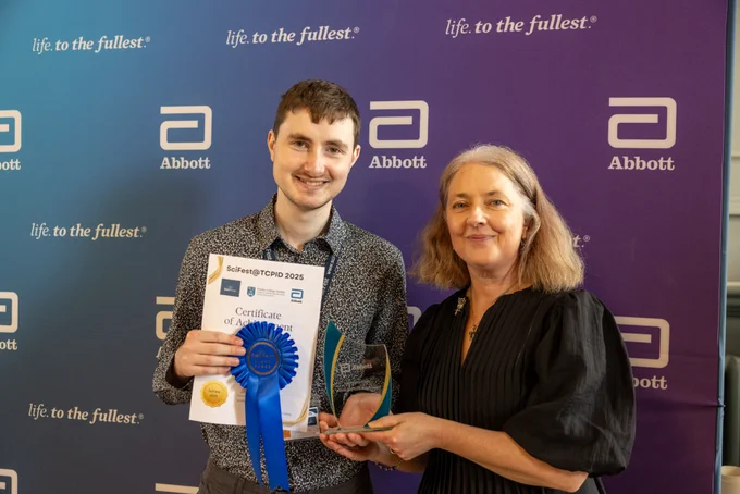 A TCPID student with his mentor from Abbott, holding a certificate and trophy in front of an Abbott banner