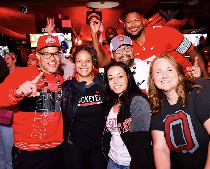 Group of people gathered in Ohio State clothing and smiling for a photo.