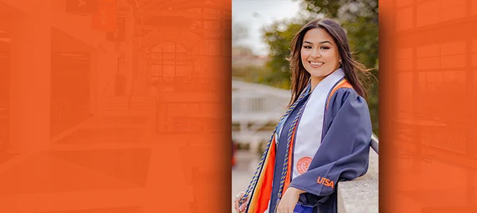 Graduate smiling in cap and gown at UTSA with a blurred campus background.