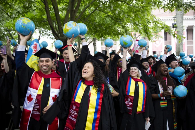 Graduates cheering and holding inflatable globes in the air during the Commencement Day Convocation at Harvard Yard.