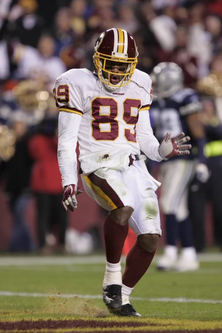 Photo of Santana Moss during a game. He is dancing after scoring a touchdown. He is wearing a burgundy helmet, white jersey, white pants, burgundy socks, black cleats and burgundy football gloves.