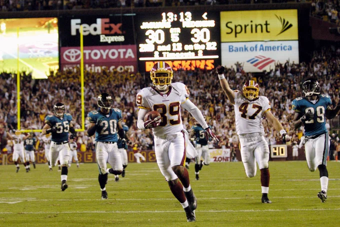 Photo of Santana Moss during a game. He is running toward the end zone. He is wearing a burgundy helmet, white jersey, white pants, burgundy socks, black cleats and burgundy football gloves.