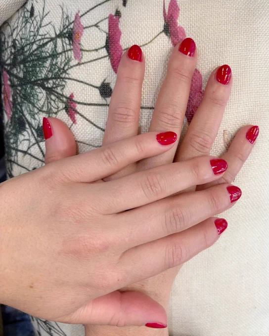Close-up of two hands with red polished nails resting on a floral fabric background.