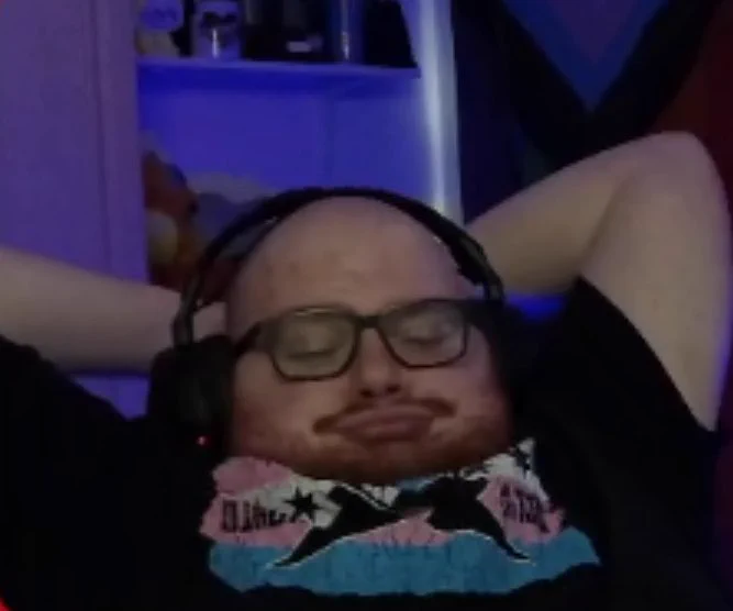 Bald man(me) leaning back in his chair with a CM Punk Trans Rights shirt on.