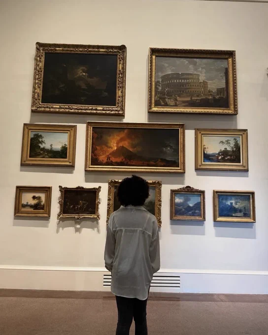 A museum visitor stands facing ten paintings displayed on a wall in VMFA's Great Hall.