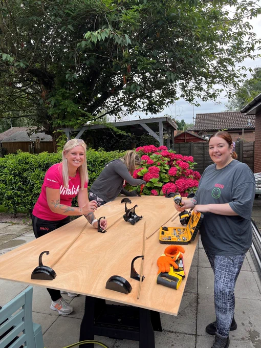 Two women stood over a plank of wood holding tools in a care home garden. 
