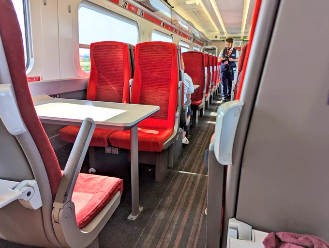 an empty train coach with red seats and a train guard walking through