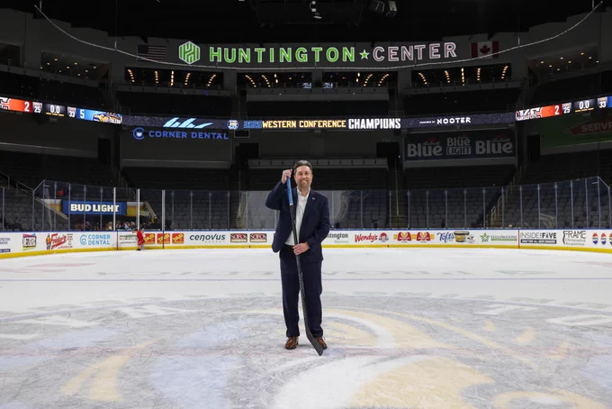 Person standing at center ice in an empty Huntington Center arena, with visible banners and logos around the rink.