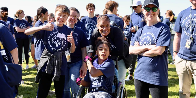 Group of smiling Special Olympics student athletes and adults standing on a field.