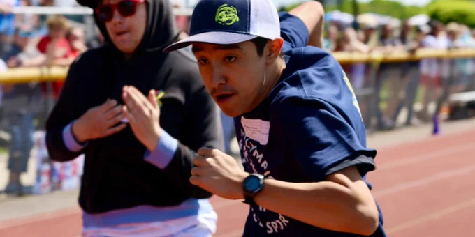 Close up of a a determined boy wearing a blue Special Olympics shirt and a blue and white  ball cap running on a track.