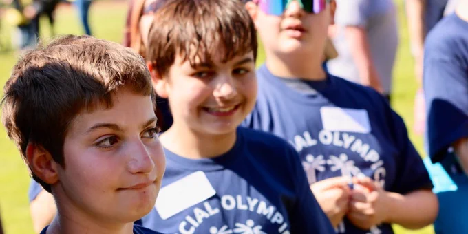 Three smiling boys in an outdoor setting wearing navy Special Olympics t shirts.