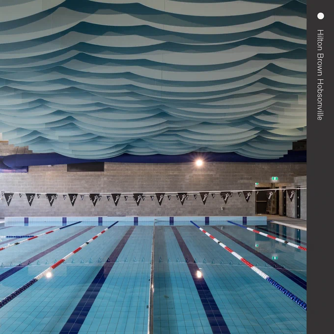Interior of the London Aquatics Centre showcasing its distinctive wave-like ceiling design above a competition swimming pool with marked lanes.