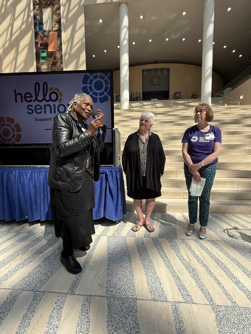 Donna and two others standing in City Hall. Donna is speaking in a mic while the others watch her speak.