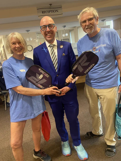 Andrew with two others standing on either side with each of them holding pickleball racquets.