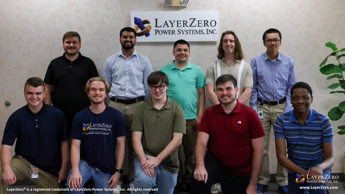 A group of 10 summer interns stand in front of a sign that has the official LayerZero logo on it. To their right is a green plant. The bottom left hand corner has text that reads, “LayerZero® is a registered trademark of LayerZero Power Systems, Inc. All rights reserved.” The bottom right hand corner has the official logo and below it reads the website name, “www.LayerZero.com”.