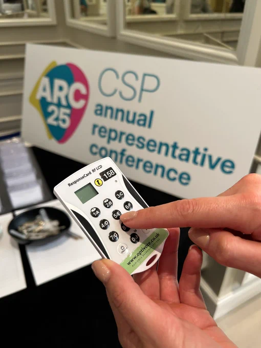Someone holding an electronic voting pad. In the background is a sign which says ‘ARC25 CSP annual representative conference’