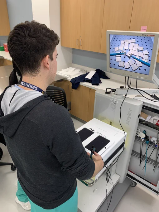 A surgery resident practices flipping over Scrabble letter tiles using laparoscopic surgery tools.