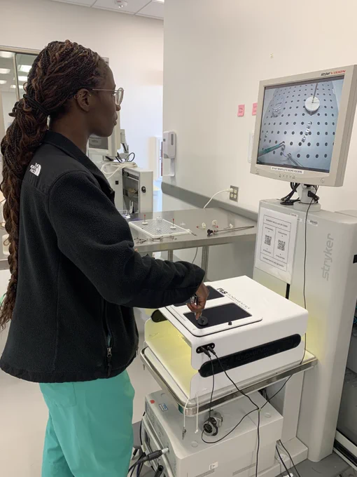 A surgery resident practices lacing beads onto a string using laparoscopic surgery tools.