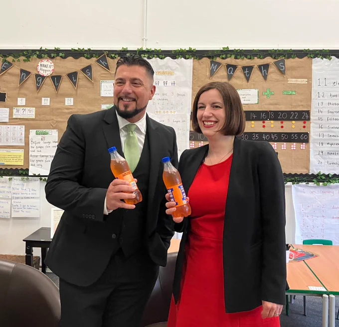 Education Secretary and Welldon headteacher stand together, holding bottles of Irn Bru and laughing.