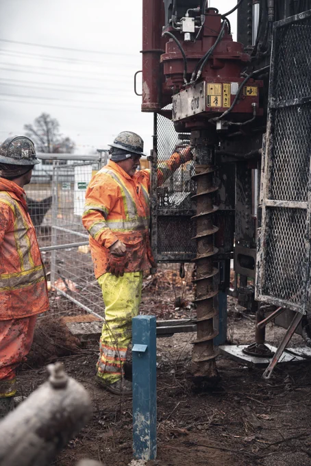Two construction workers operating a large drilling rig at the Walmsley Brook construction site.