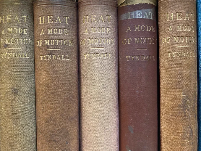 Photo of spines of 5 books on a shelf (editions of"Heat A Mode of Motion" by John Tyndall).