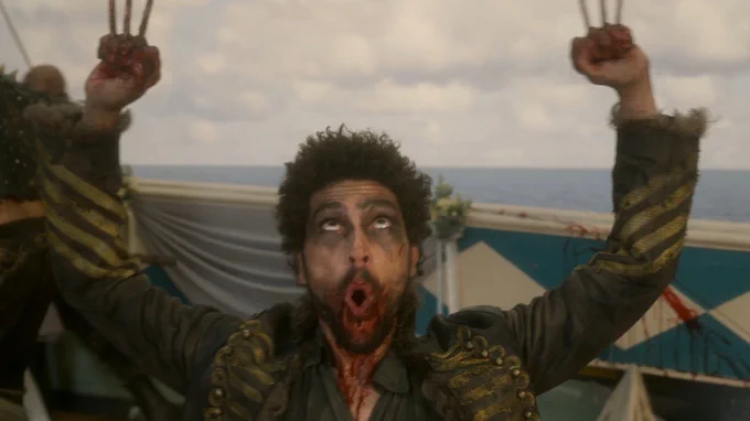 Joel Fry dressed as Frenchie from Our Flag Means Death wearing a blue jacket and claws on his hands.