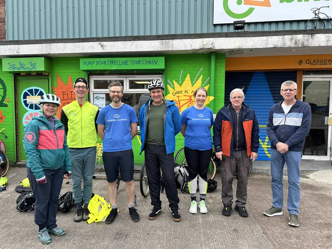 Josh and Nina from Cycling Scotland stand together with Ali and Laura from Visibility Scotland and three service members outside the Bike for Good hub in Glasgow. 