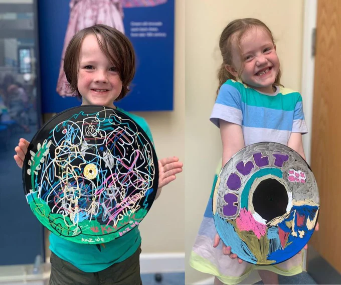 Two children holding vinyl records they have decorated using posca pens in a Vinyl Graffiti workshop.