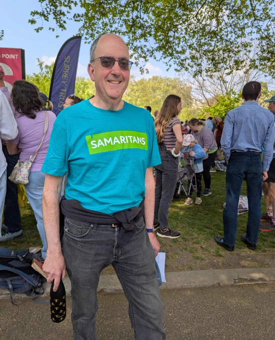 A photo of David in his Green Samaritans t-shirt and grey jeans. He's smiling at the camera and wearing sunglasses.