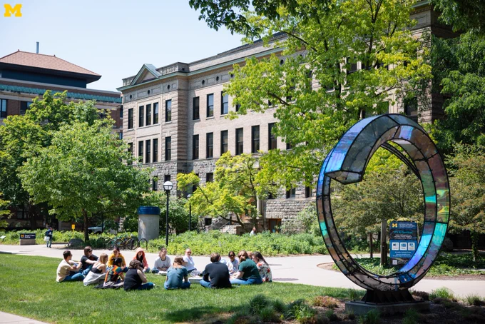 U-M students sitting in a circle near the Arriving Home Sculpture