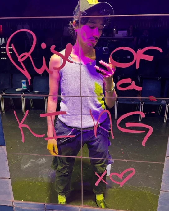 Vico Ortiz standing on a stage in front of chairs in front of a mirror with Rise of a King X<3 written in red paint on the mirror