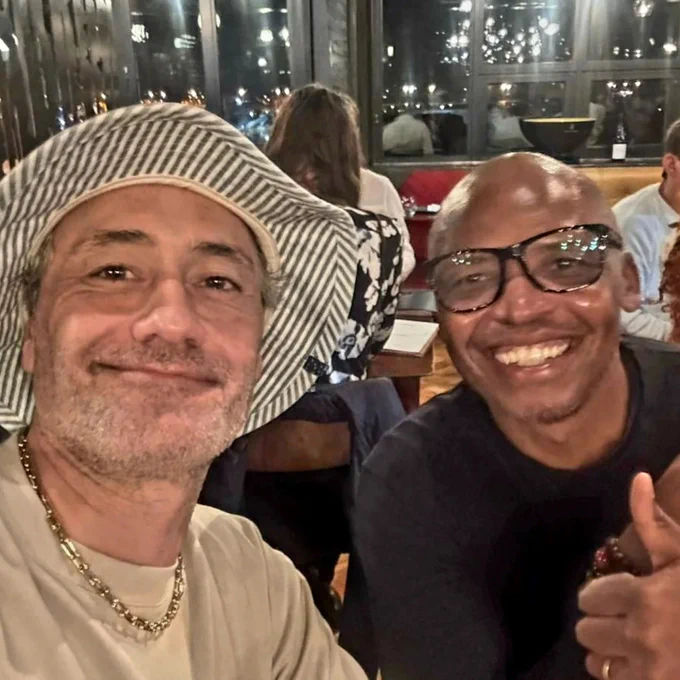 Taika sitting next to NVFilmStudiosAfrica's Chairman Simo Kubheka in a restaurant.

