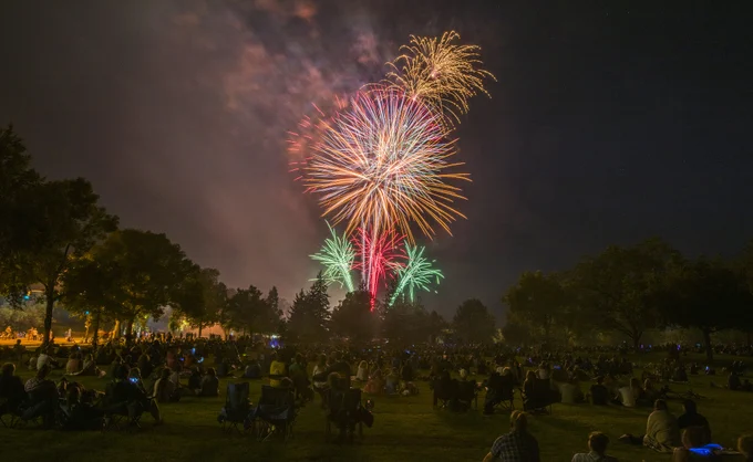 Red, green, orange and yellow fireworks over people seated in lawn chairs