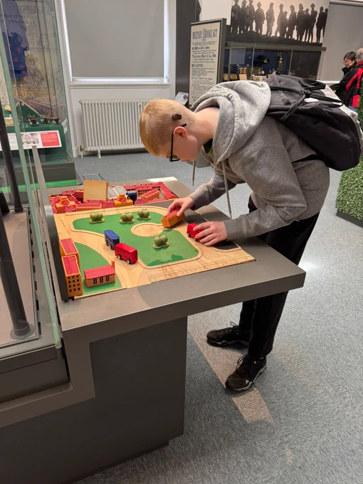A young man wearing a cochlear implant bending over a table, exploring a wooden cars. 