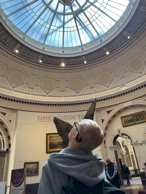 A young man wearing a cochlear implant looking up at the glass roof of an art gallery. 