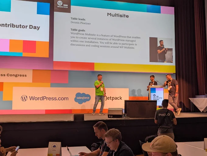 Dennis from Syde stands on stage at WordCamp Europe Contributor Day 2025, presenting the WordPress Multisite table. A large screen behind him displays the Multisite table details, including his name as table lead. Other speakers and attendees are visible, with the WordPress, Salesforce, and Jetpack logos in the background.